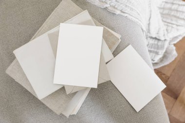 Set of blank greeting cards, invitations and craft envelopes mockups. Old books on linen sofa with cotton throw.Blurred wooden floor background, home office, elegant stationery. Artistic display.