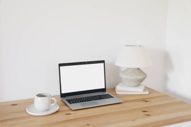 Elegant workspace composition. Cup of coffee, rustic vase and books. Laptop mockup on wooden table. White wall background, elegant Scandinavian interior, neutral colors. Blogger, home office.