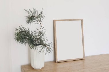Noel İskandinav iç mimarisi. Minimum kış sanatsal kompozisyonu. Boş dikey ahşap çerçeve modeli. Masada, masada, bej duvarda vazoda çam ağacı dalları var. Boş kopyalama alanı.