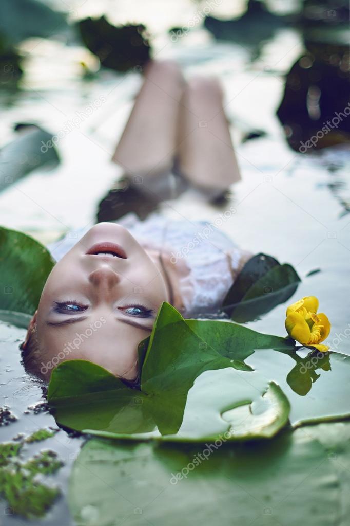 Beautiful girl lies in the water among the flowers
