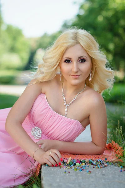 Mooie blonde meisje in een roze jurk in het park — Stockfoto