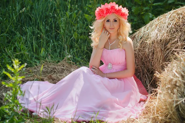 Chica rubia bonita en un vestido rosa y con corona de flores en el — Foto de Stock