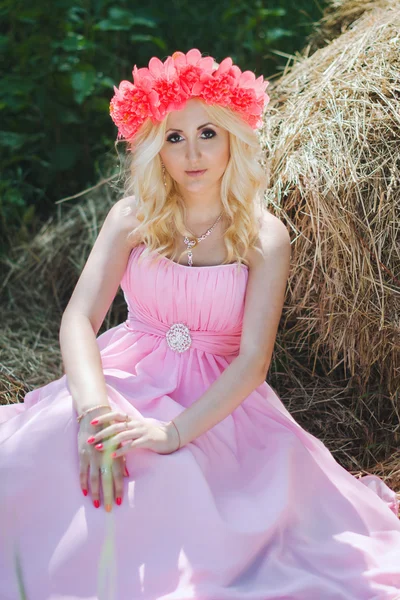 Hübsche blonde Mädchen in einem rosa Kleid und mit Blumenkranz in der — Stockfoto