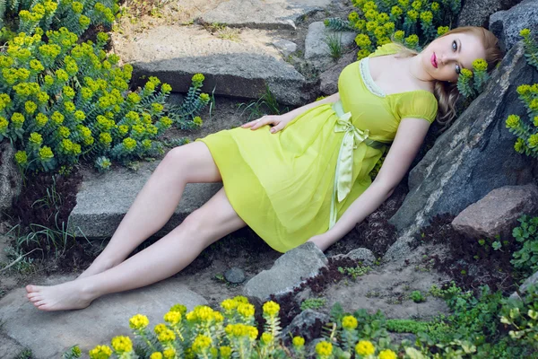Hermosa chica rubia acostada entre las flores de primavera — Foto de Stock