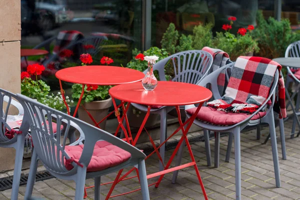 Empty chairs in outdoor cafe or restaurant. Red and gray metallic tables and chairs at sidewalk cafe. Autumn in city, plaids on chairs and tables of a street cafe