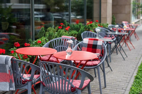 Leere Stühle im Café oder Restaurant im Freien. Rote und graue metallische Tische und Stühle im Straßencafé. Herbst in der Stadt, Plaids auf Stühlen und Tischen eines Straßencafés — Stockfoto