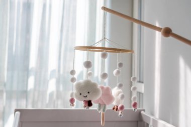 Gülümseyen bulutlar ve karlı bebek beşiği. Çocuklar yeni doğan beşiğin üstünde el yapımı oyuncaklar. Keçeden yapılmış ilk bebek çevre dostu oyuncaklar ve aydınlık odada asılı duran ahşap