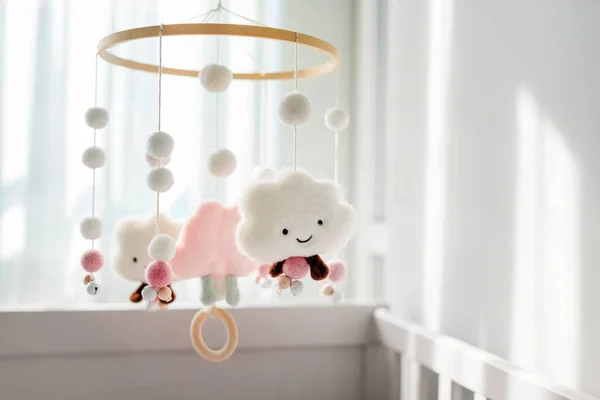 Baby crib mobile with smiling clouds and snow. Kids handmade toys above the newborn crib. First baby eco-friendly toys made from felt and wood hanging in light room