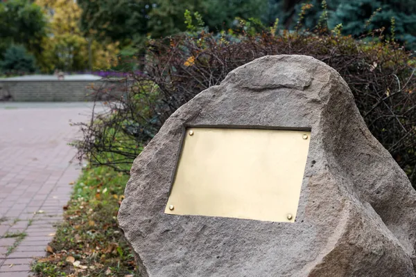 Plaque blanche sur la pierre. Plaque commémorative en bronze dans le parc. Panneau vide sur le mur. — Photo