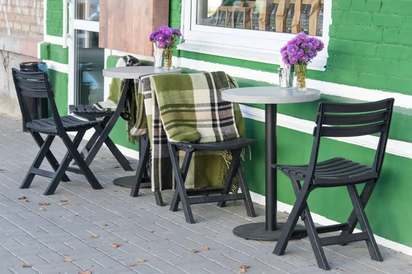 Пустые стулья в открытом кафе или ресторане. Деревянные столы и стулья в кафе на тротуаре. Осень в городе, пледы на стульях и столах уличного кафе — стоковое фото