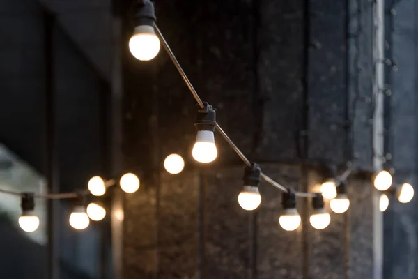 Blurred background, backyard illumination, light in the evening garden, electric lanterns with round diffuser. Lamp garland of light bulbs, illuminate night scene. — Fotografia de Stock