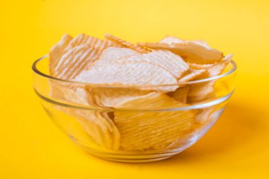 Sarı arka planda cam kasede patates cipsi. Sağlıksız yiyecek, cips, parti yemeği, fast food konsepti, mesaj için boş yer