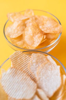 Sarı arka planda cam kaselerde patates cipsi. Sağlıksız yemekler, cipsler, parti yemekleri, fast food konsepti.