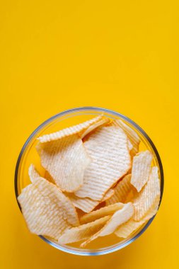 Sarı arka planda cam kasede patates cipsi. Sağlıksız yiyecek, cips, parti yemeği, fast food konsepti, mesaj için boş yer