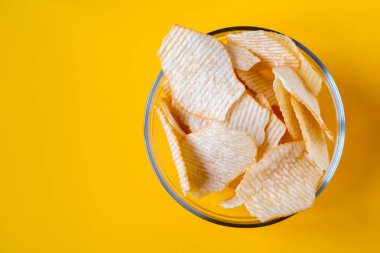Sarı arka planda cam kasede patates cipsi. Sağlıksız yiyecek, cips, parti yemeği, fast food konsepti, mesaj için boş yer