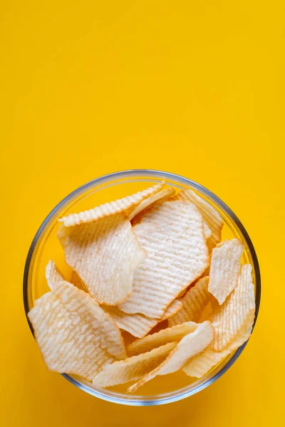 Potato chips in glass bowl on yellow background. Junk unhealthy food, chips, party food, fast food concept, free space for text — Foto Stock