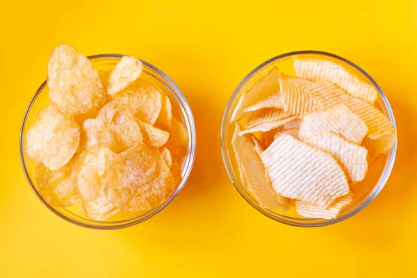 Sarı arka planda cam kasede patates cipsi. Sağlıksız yiyecek, cips, parti yemeği, fast food konsepti, mesaj için boş yer