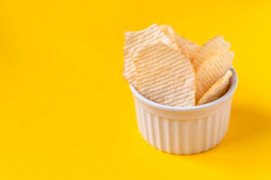 Beyaz seramik kasede sarı arka planda patates cipsi. Sağlıksız yiyecek, cips, parti yemeği, fast food konsepti, mesaj için boş yer