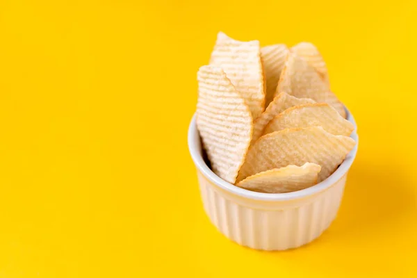 Riffled potato chips in white ceramic bowl on yellow background. Junk unhealthy food, chips, party food, fast food concept, free space for text — Stock Photo, Image