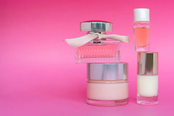 Lahvička z růžového skla, krém na obličej a kosmetický výrobek na růžovém pozadí. Lahvička ženského parfému, péče o pleť, kosmetické, volný prostor pro text. — Stock fotografie