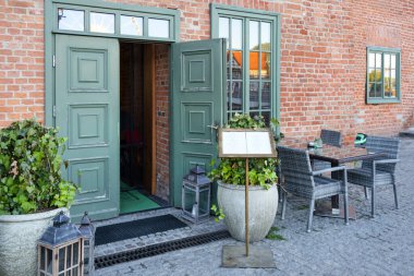 Restoranın girişinde menü var. Modern ve rahat kafe ya da açık verandada masaları ve sandalyeleri olan bar cephesi