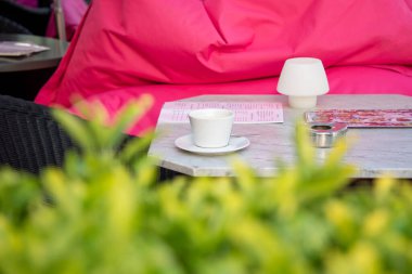 Cup of coffee on outdoor cafe table. Outdoor restaurant or cafe table with coffee cup surrounded with green plants in summertime