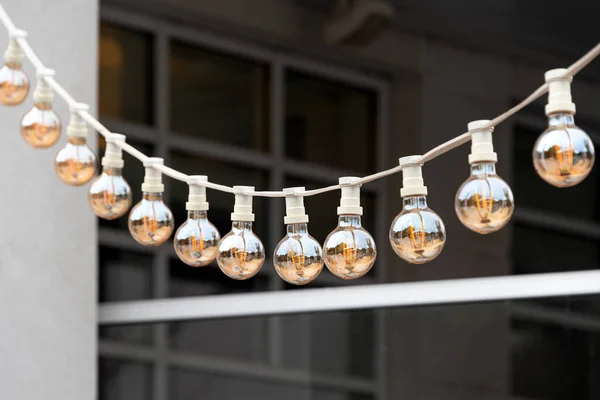 Light garland on the street at daylight. Decoration of the street with vintage Edison bulbs garland, festive city decorations for cafe and restaurant, celebrating, lights as exterior decor.