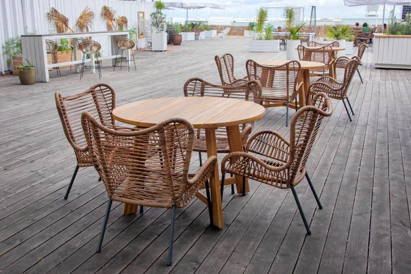 Outdoor cafe with wicker furniture and wooden tables. Empty tables in outdoor sidewalk cafe or restaurant. Touristic setting, cafe table setting.