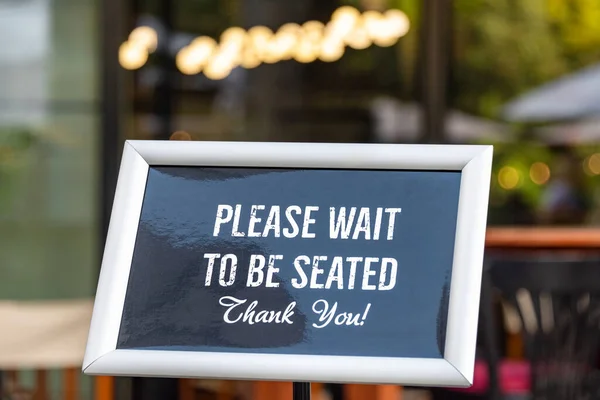 Please wait to be seated sign standing at the front of a restaurant. Sidewalk cafe hostess stand with message signboard for clients