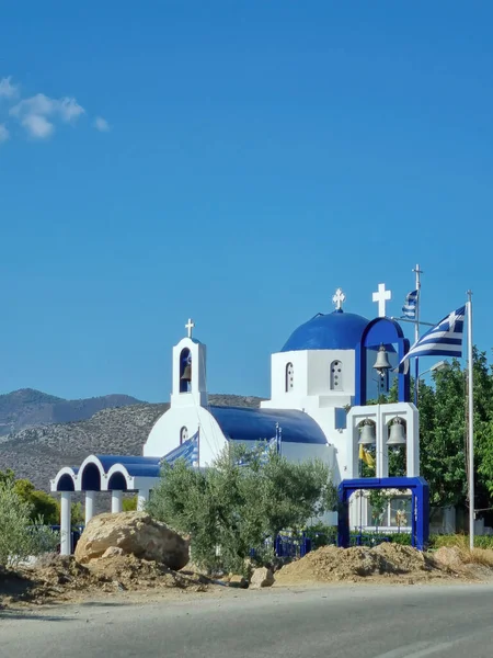 Santorini island, Greece. Greek flag waving on white orthodox church with blue dome against blue clear sky background, vertical photo