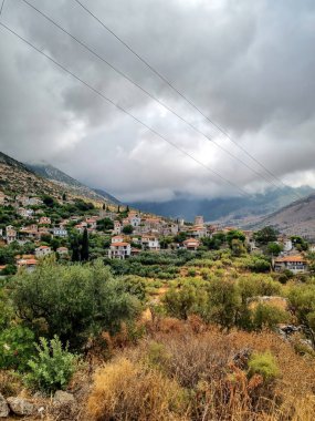 Yunanistan 'ın Peloponnese, Lagkada dağlarındaki kara bulutların altında gün batımında aydınlanan Yunan köyü