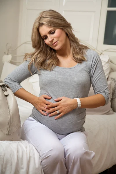 임신한 여자 수축 통증으로 침대에 앉아서 쉬고 그녀의 배에 손을 — 스톡 사진