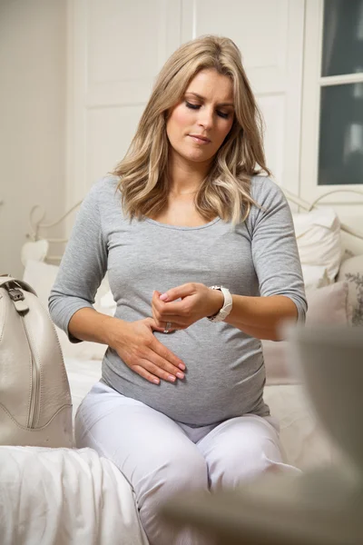 Vrij zwangere vrouw met hand op buik kijken horloge en timing contractie pijnen Rechtenvrije Stockafbeeldingen