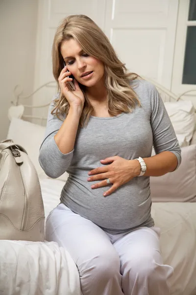 Zwangere vrouw op zoek angstig praten over telefoon en houden haar buik Stockafbeelding
