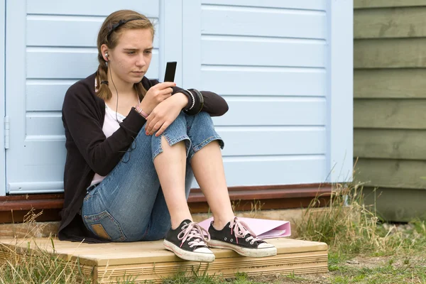 Teenage girl sitting by beach hut listening to music — Stock Photo, Image