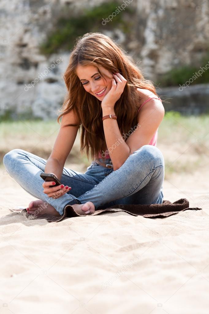 Beautiful woman sitting on beach towel using mobile phone