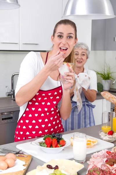 Молодая женщина готовит и ест со своей матерью на кухне  - — стоковое фото