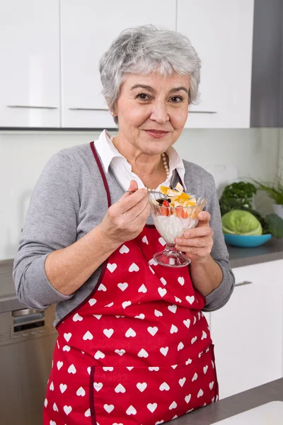 Mujer mayor cocinar y comer en la cocina — Foto de Stock