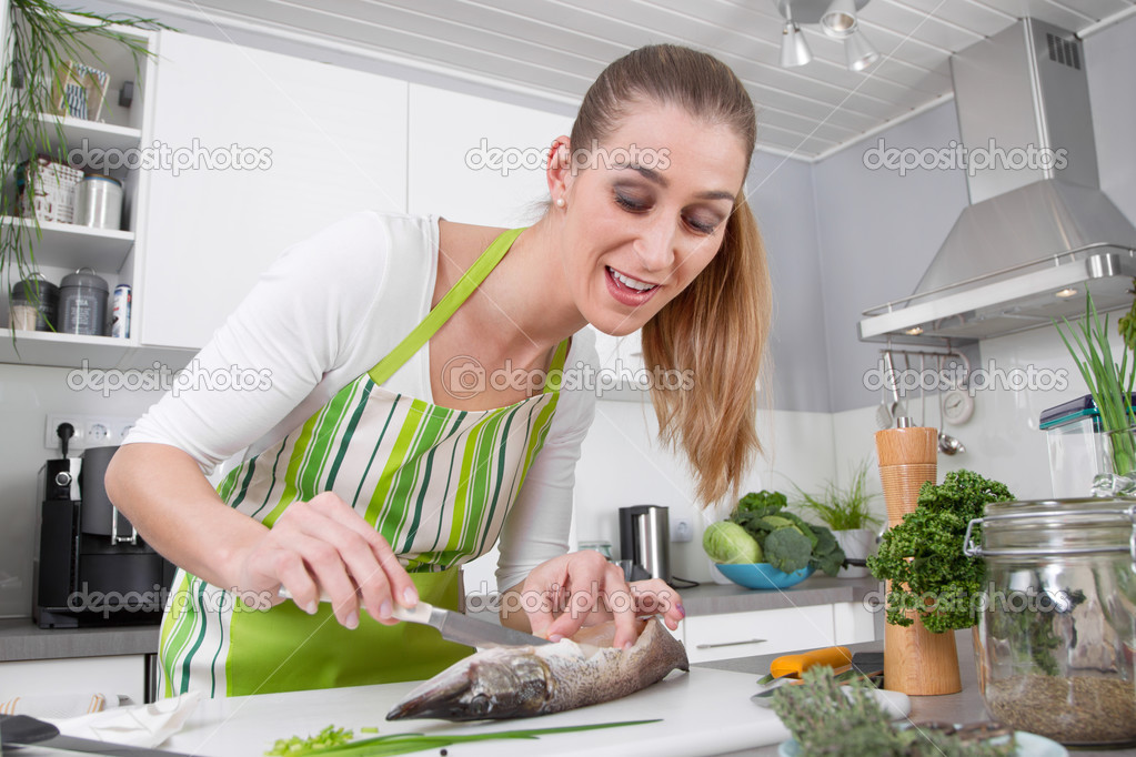 Young woman cooking fish in the kitchen