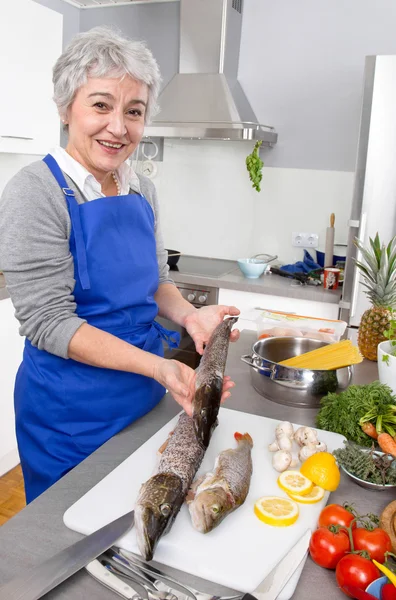 Mulher sênior preparando peixe na cozinha — Fotografia de Stock