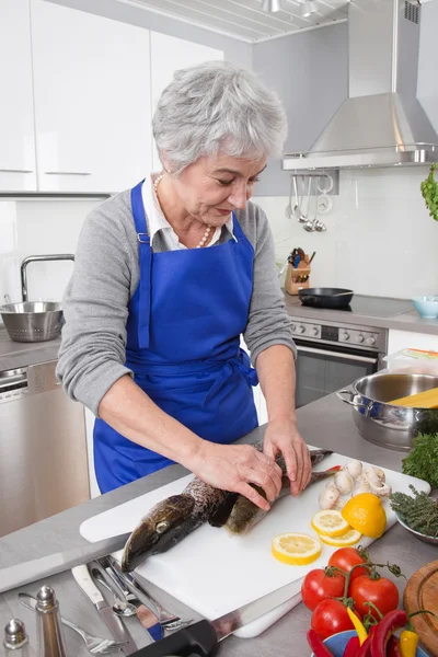 Ανώτερος γυναίκα προετοιμασία ψάρια στην κουζίνα — Φωτογραφία Αρχείου