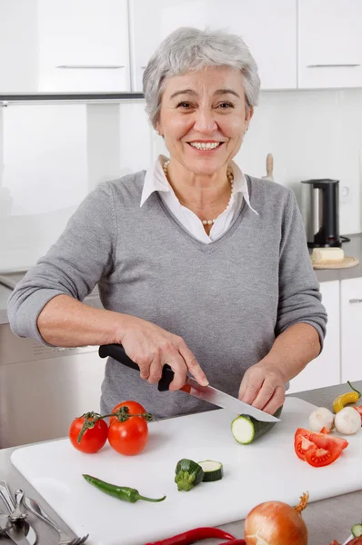 Пожилая женщина режет овощи на кухне — стоковое фото
