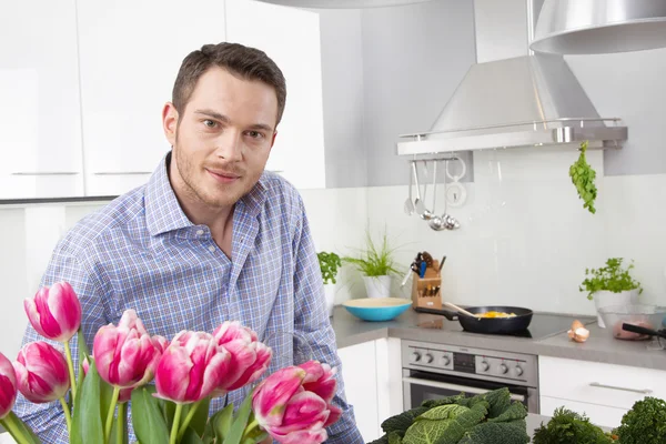 Šťastný muž pózuje v kuchyni s růžové tulipány — Stock fotografie