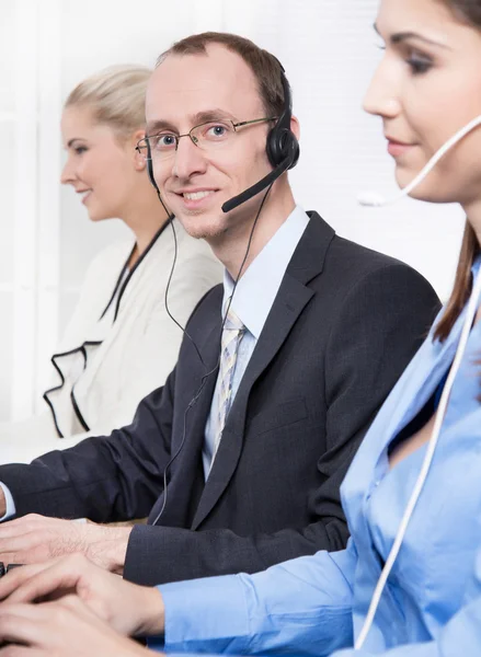 Telesales o helpdesk team - uomo utile con auricolare sorridente alla scrivania - uomo e donna - call center — Foto Stock