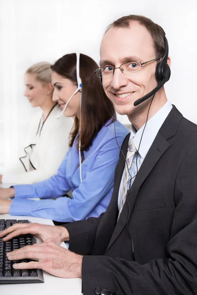 Telesales o helpdesk team - uomo utile con auricolare sorridente alla scrivania - donna di gruppo e uomo — Foto Stock