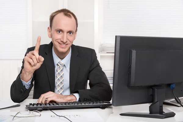 Portrait of a smiling businessman showing his index finger sitting at desk Royalty Free Stock Photos