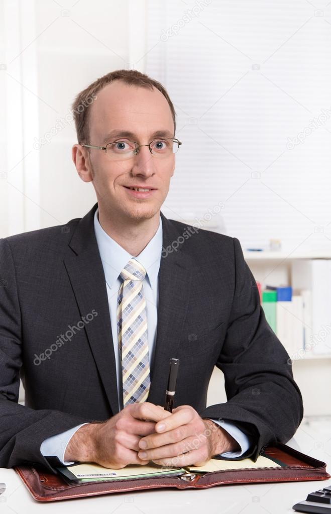 Portrait of a young businessman sitting at desk in suit and tie