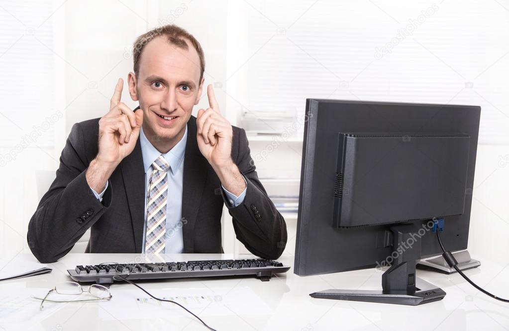 Smiling business man with fingers up sitting at office.