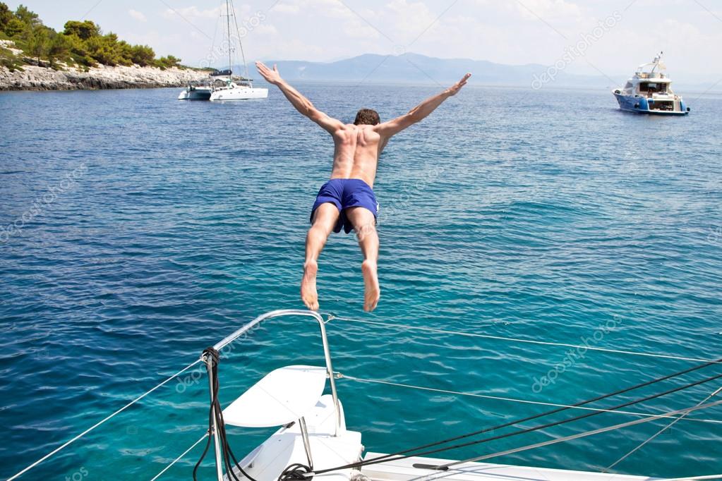 Young man jumping from a sailing boat.