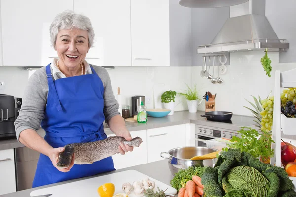 Senior eller äldre kvinna med grå hår matlagning i köket - färskt — Stockfoto